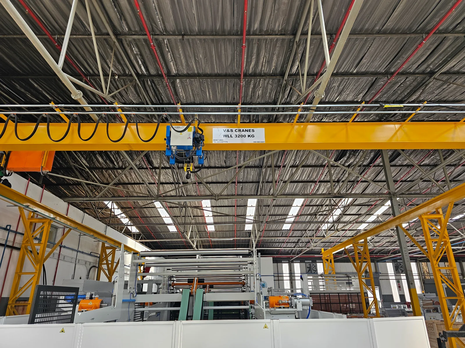 Yellow V&S overhead crane, hoist and lifting hook beneath the steel roof of a factory
